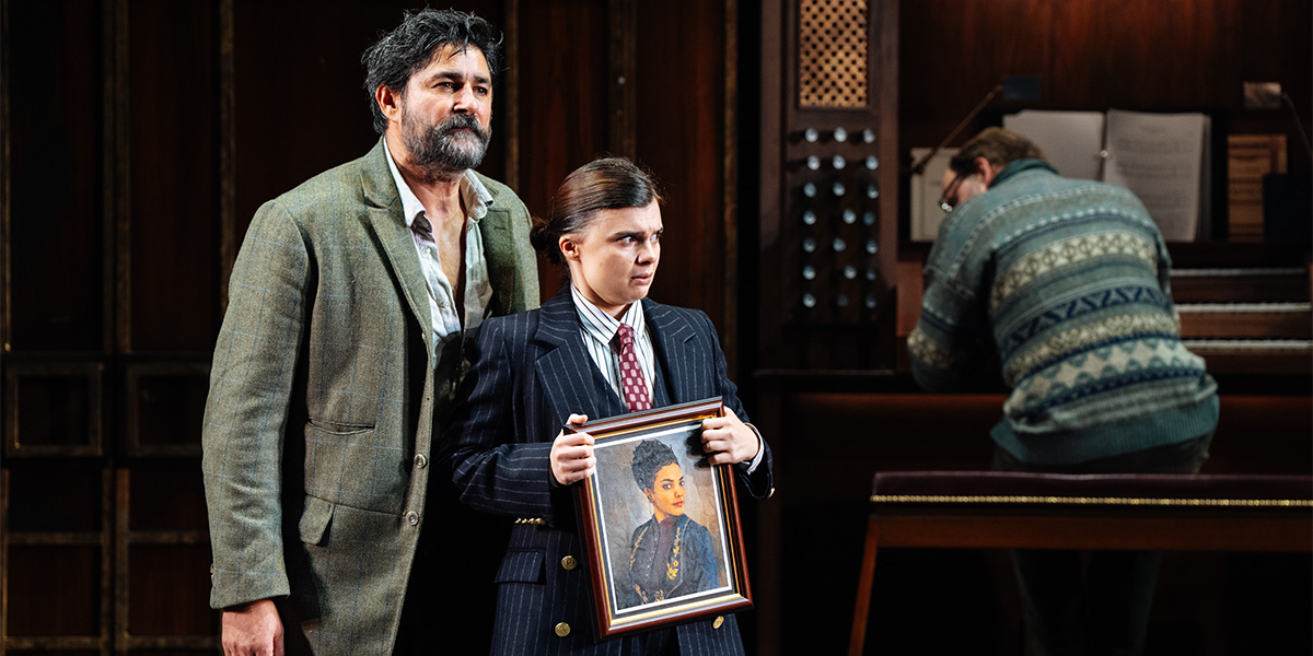 A scene from Twelfth Night featuring an actor holding a photograph in a frame, with another actor standing directly behind them