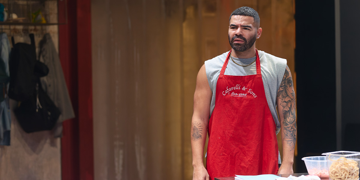 Ash Hunter, wearing a red apron, looks concerned while standing at a counter with meat.