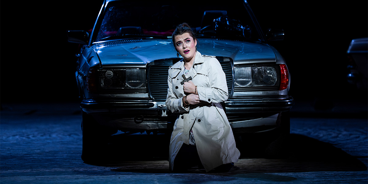A woman in a red dress sings passionately on stage, with dramatic lighting and a dark background.