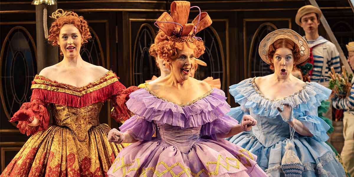 Bethan Langford, Mel Giedroyc, and Deborah Davison pose together, smiling, in colourful costumes for ENO's HMS Pinafore.