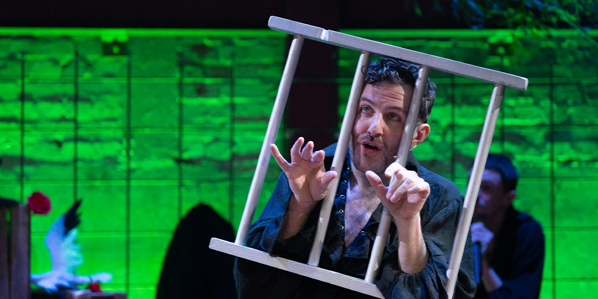 A person holds bars which look like prison bars, illuminated by green lighting.