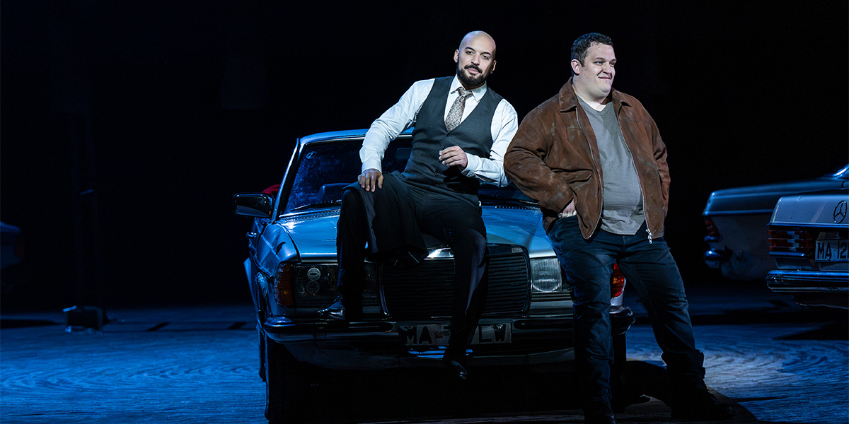 Cory McGee and John Findon perform on stage in vibrant costumes, with dramatic lighting and set design.