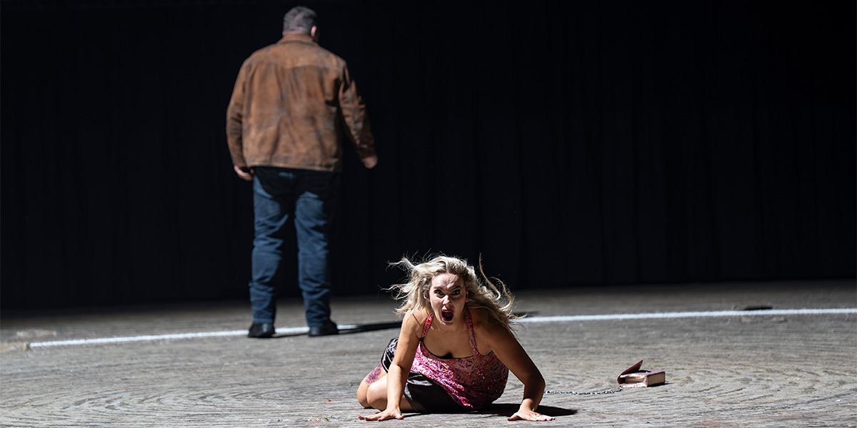 A man and woman perform a dramatic duet on stage, dressed in vibrant costumes against a dark backdrop.