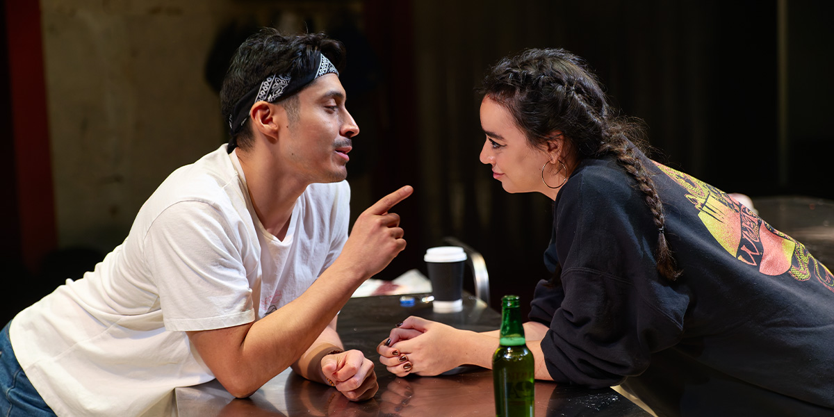 Marcello Cruz and Mithra Malek pose together, smiling, in front of a vibrant backdrop featuring meat products.