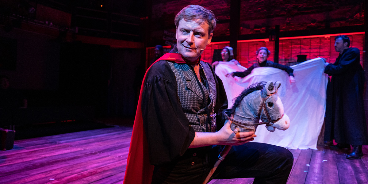 A person wearing a red cloak rides on a toy horse.