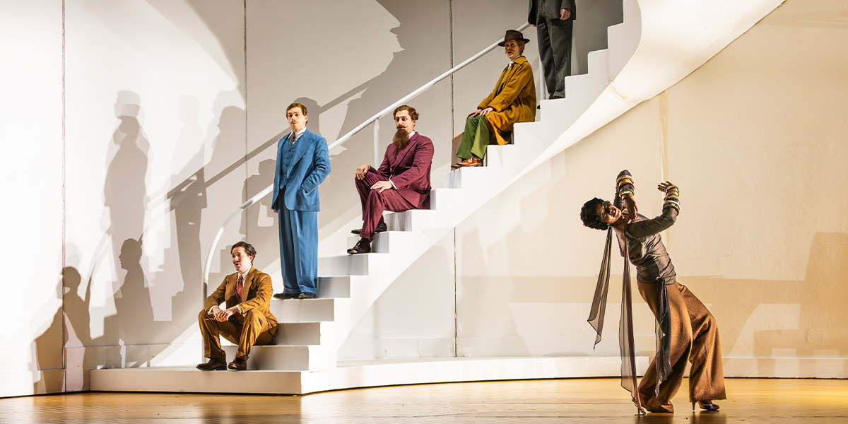 The cast of ENO's Partenope 2025 poses together, wearing vibrant costumes against a theatrical backdrop.