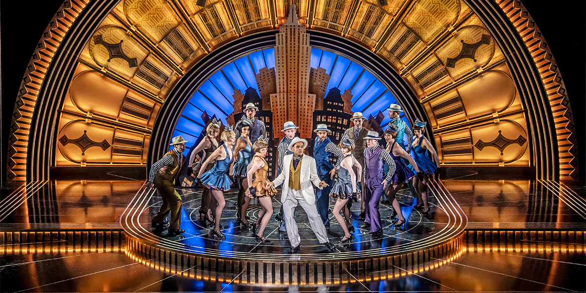 A group of people in formal attire stands together, smiling on stage.