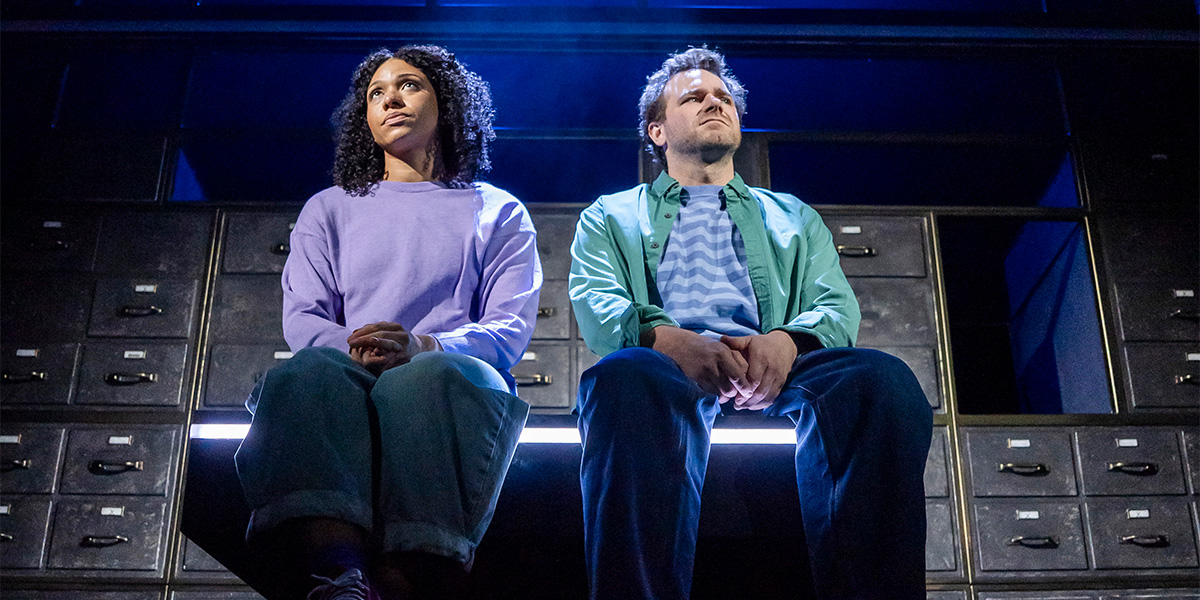 Four actors in vibrant costumes perform on a dimly lit stage, with dramatic lighting highlighting their expressions.