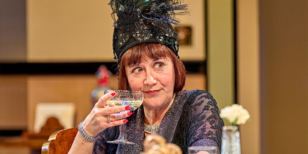Alexandra Gilbreath as Jane Banbury, wearing a period costume, stands on stage with dramatic lighting.
