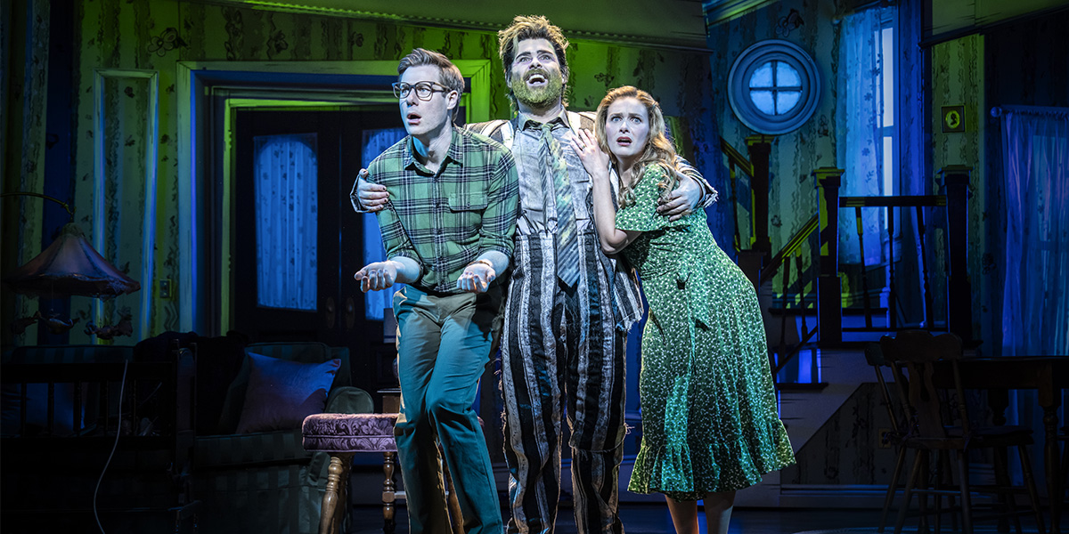 A performer in a striped suit and green wig poses dramatically on stage during Beetlejuice The Musical.
