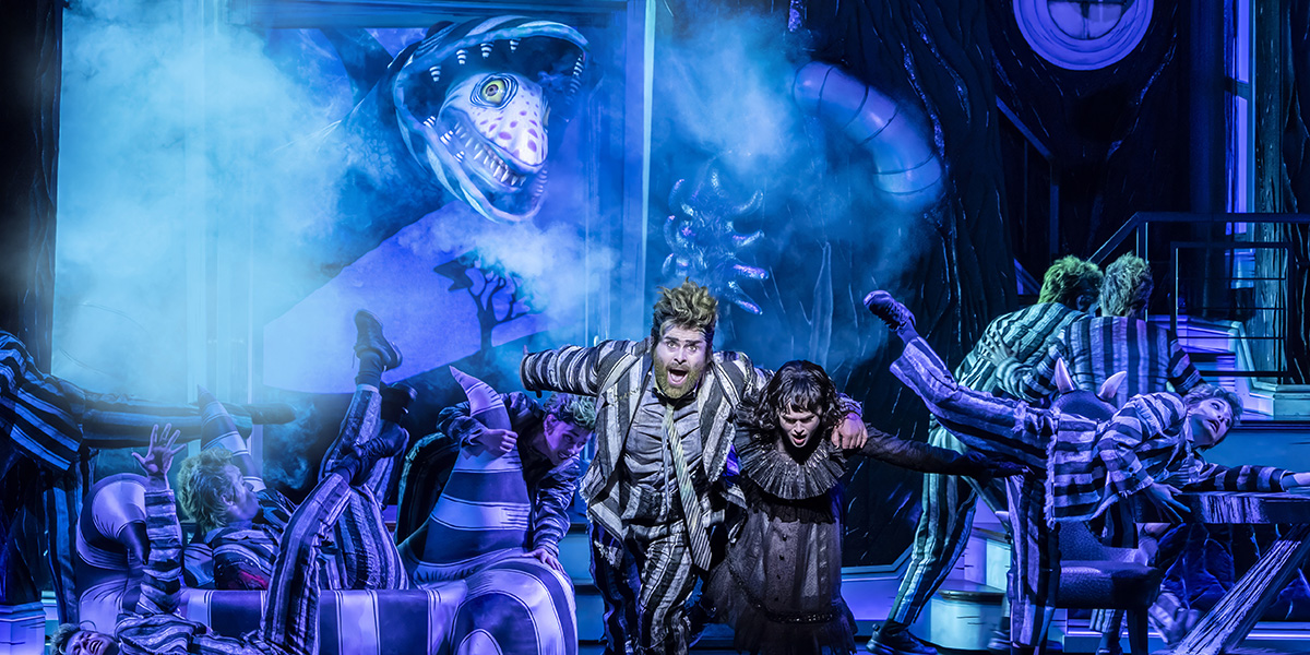 A scene from Beetlejuice The Musical featuring vibrant costumes and theatrical lighting, with actors performing energetically.