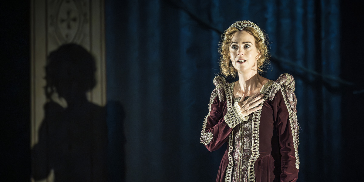 A woman in a flowing blue dress stands gracefully, surrounded by soft, natural light and greenery.