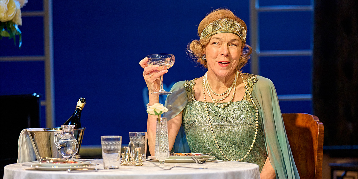 Janie Dee as Julia Steroll, wearing a flowing dress, stands centre stage with dramatic lighting.