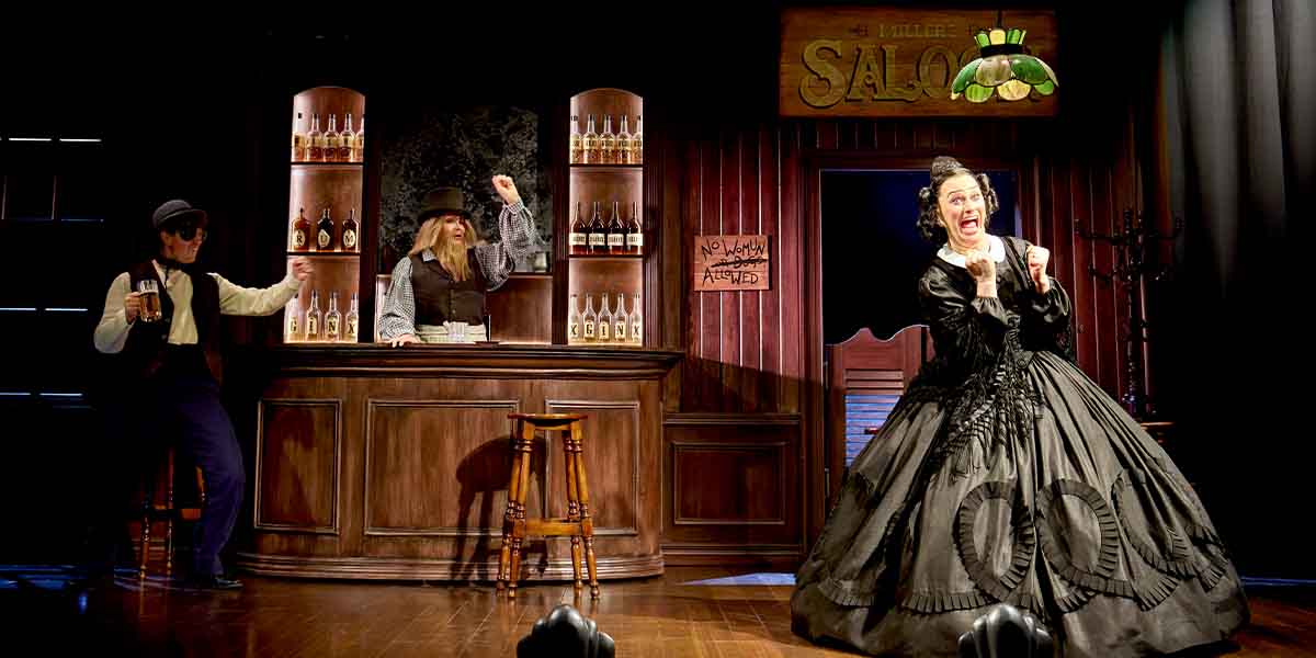 Jinkx Monsoon as Mary Todd Lincoln performs dramatically in a saloon, with Oliver Stockley and Kate O'Donnell nearby.