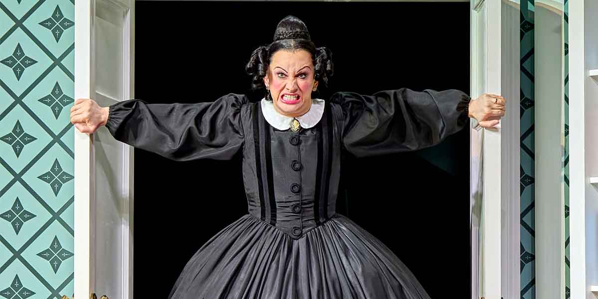 Jinkx Monsoon, portraying Mary Todd Lincoln, dramatically bursts through a doorway, wearing a black dress.