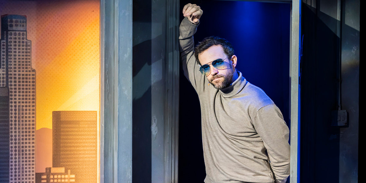 Iffy Mizrahi poses confidently, wearing a stylish outfit with vibrant colours, against a blurred background.