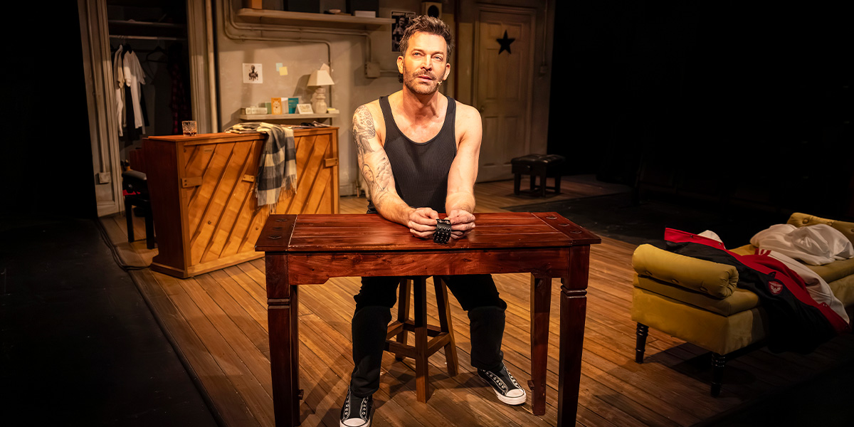 Levi Kreis performs on stage, wearing a black shirt, with bright lights and a cheering audience in the background.