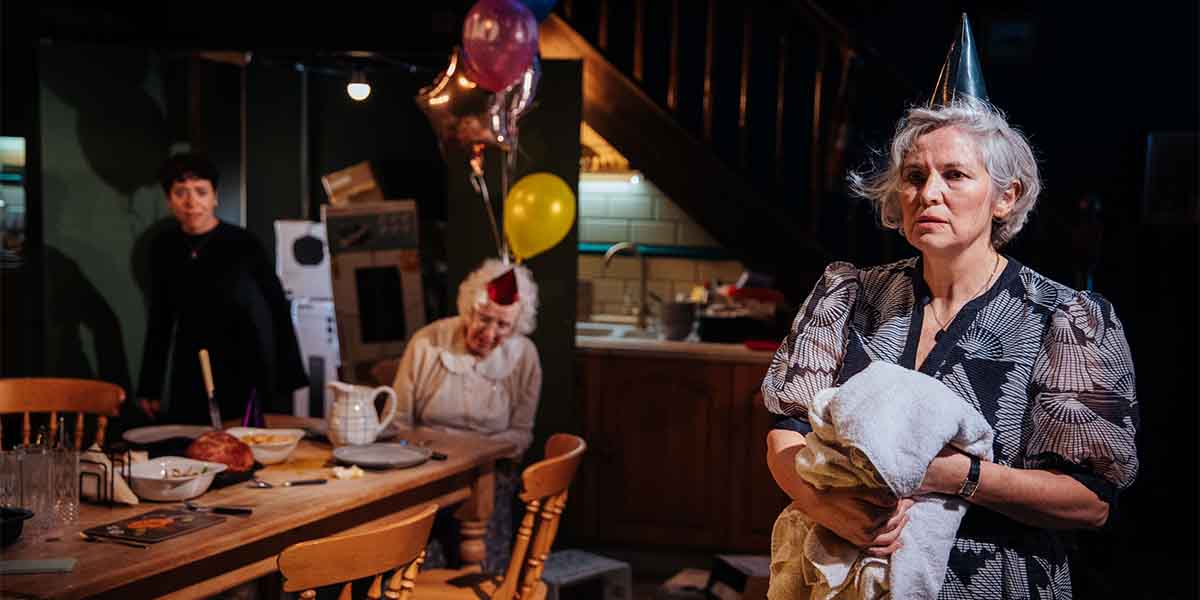 Caoimhe Farren, Julia Dearden, and Andrea Irvine in a tense scene with balloons and a cluttered table.