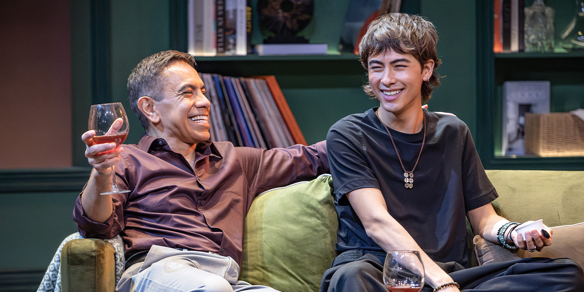 Two people sit on a green sofa laughing.