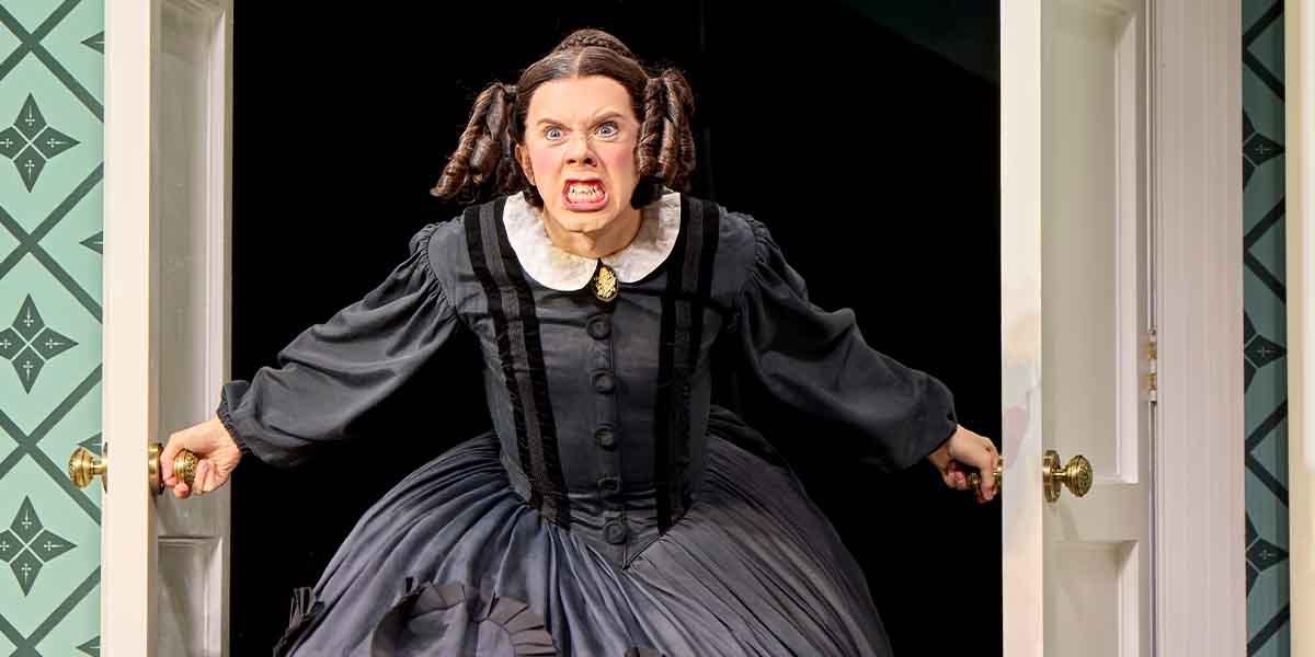Cole Escola, portraying Mary Todd Lincoln, angrily bursts through a doorway, wearing a dark dress with a white collar.