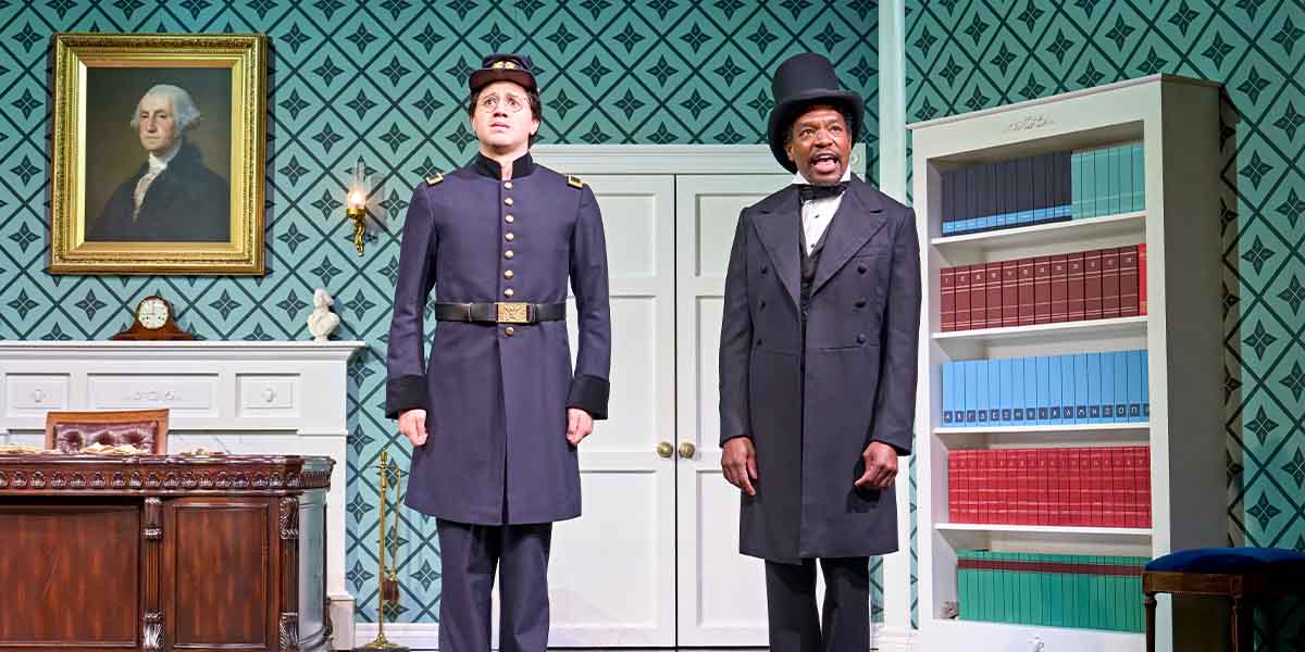 J.R. Ballantyne and Syrus Lowe perform on stage, dressed in period costumes, against a patterned backdrop.