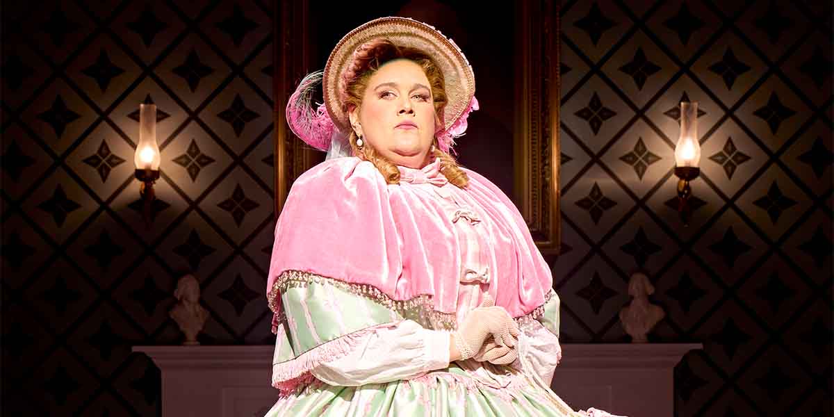 Lucy Frederick, dressed in a pink gown and bonnet, poses confidently against a patterned backdrop.