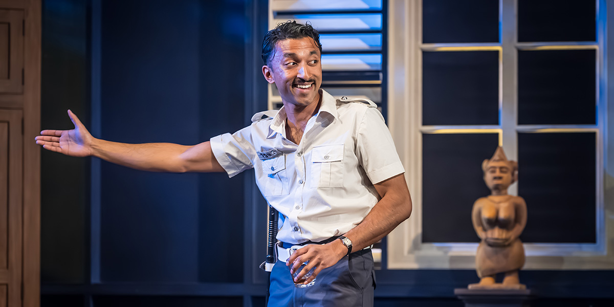 Shane David-Joseph gestures enthusiastically while wearing a light-coloured uniform, with a wooden statue in the background.