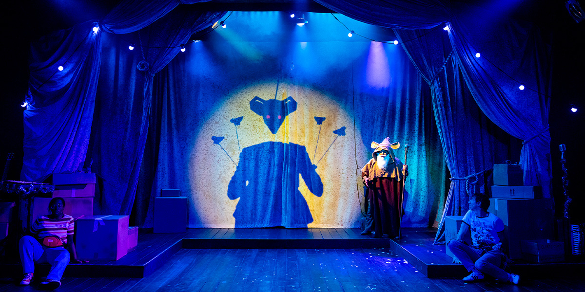 A ballet dancer in a pink tutu performs an arabesque on stage, with festive decorations in the background.