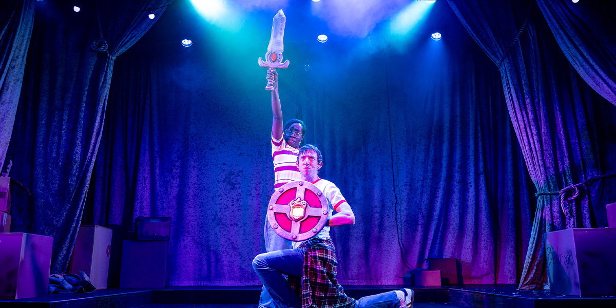 A ballet dancer in a pink tutu performs an elegant pose on stage, surrounded by festive decorations.