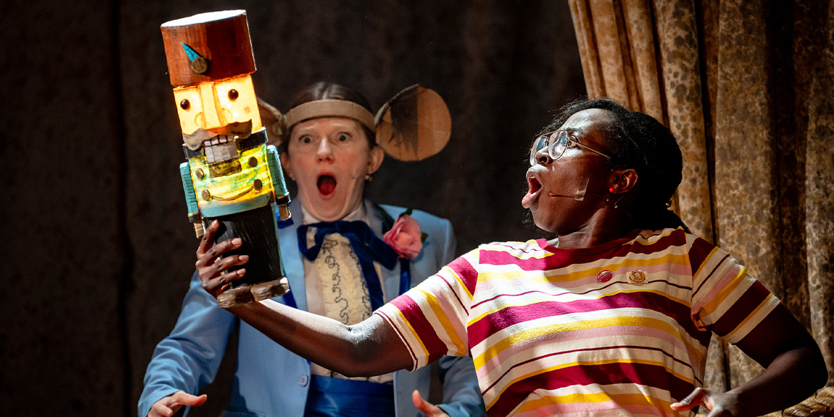 A dancer in a pink tutu performs a graceful pose on stage, surrounded by festive decorations and soft lighting.