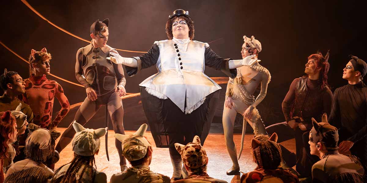Elliot Broadfoot as Bustopher Jones performs centre stage, surrounded by other costumed performers in a theatrical setting.