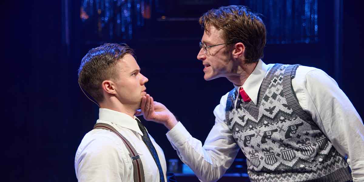 Ryan Heenan and Hugo Bolton perform a tense scene, with Bolton gripping Heenan's chin, under dramatic lighting.