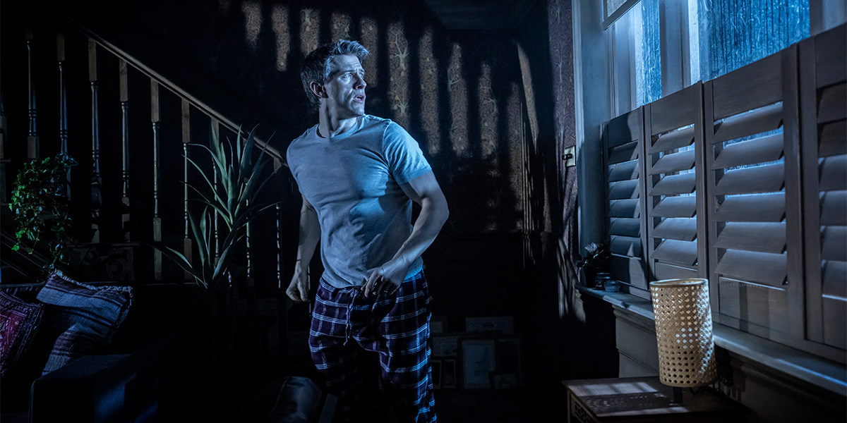 a person stands in a dimly lit room, looking intently at a flickering light source.