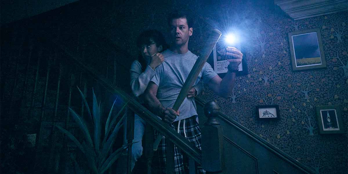 Ty Fanning as James holds a flashlight, while Ami Okumura Jones as Lou clings to him on stairs.