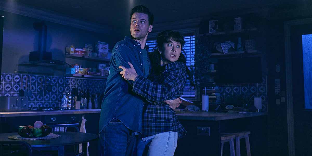 Ty Fanning as James and Ami Okumura Jones as Lou, embracing in a dimly lit kitchen.