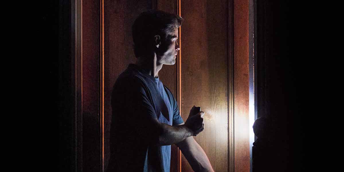 Ty Fanning as 'James' holds a flashlight, illuminating a wooden door in a dark setting.