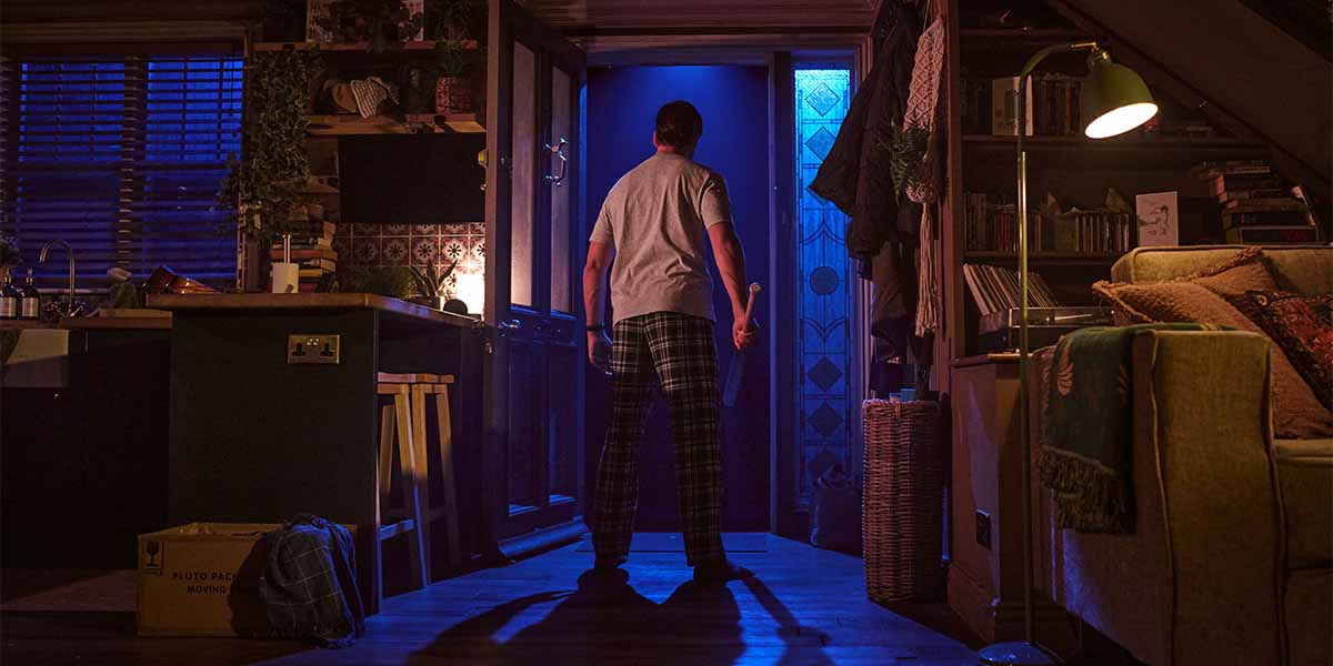 Ty Fanning as James stands in a dimly lit room, facing an open door with blue light.