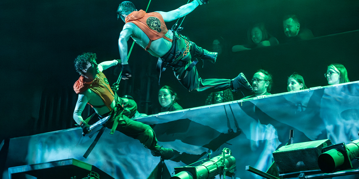 A dramatic stage scene from "The Hunger Games: On Stage," featuring actors in elaborate costumes and intense expressions.