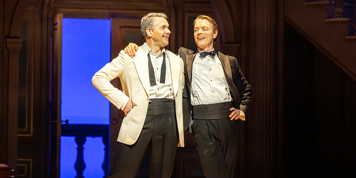 Julian Ovenden as Dexter Haven and Freddie Fox as Mike Connor pose together, smiling, in formal attire.