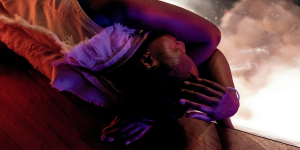 Yewande stands in a vibrant, textured setting, surrounded by abstract shapes and colours, conveying a sense of depth.