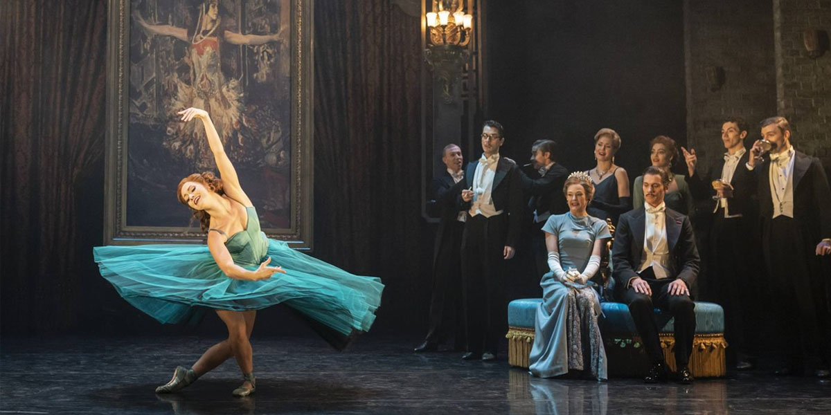 A dancer in red shoes performs on stage, surrounded by dramatic lighting and a dark backdrop.