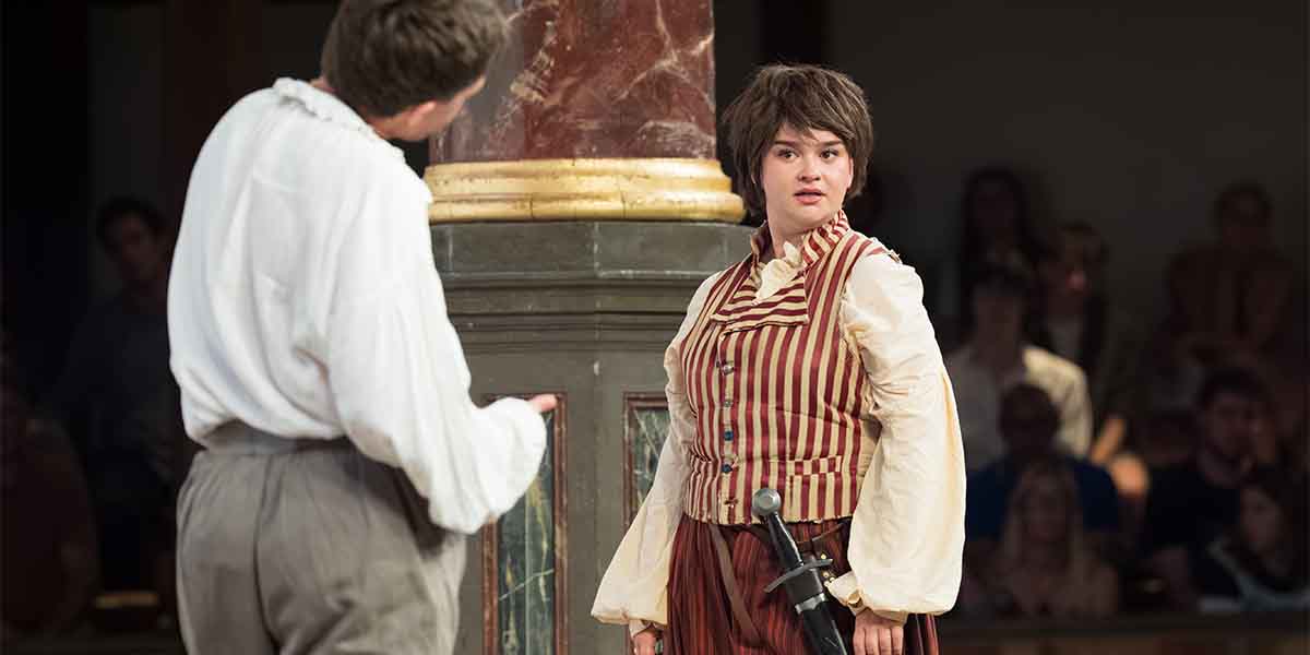 Charlie Josephine as Orlando and Lola Shalam as Rosalind, engaged in dialogue, with a sword visible at Rosalind's side.