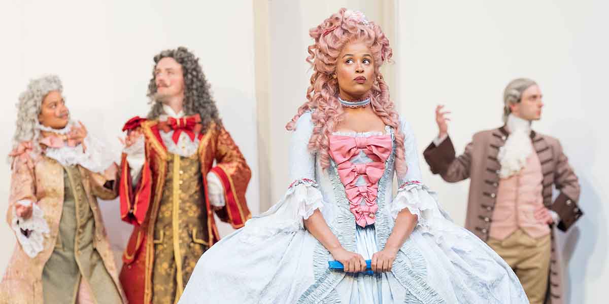 Gracie Oddie-James as Celia, wearing a blue and pink gown, stands centre stage with three male actors.
