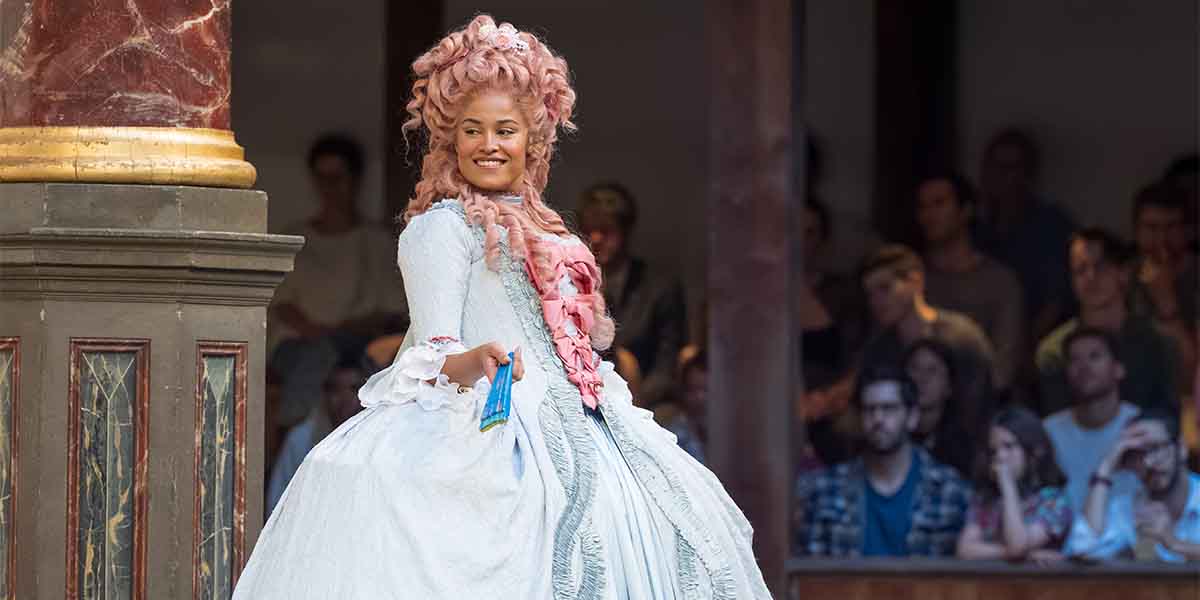 Gracie Oddie-James as Celia wears a white gown with pink accents, smiling at an audience.