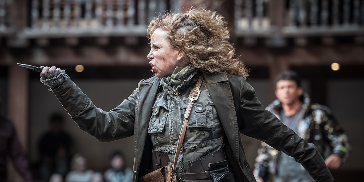 Michelle Terry portrays Mother Courage, wearing period costume, with a dramatic expression on stage at Shakespeare's Globe.