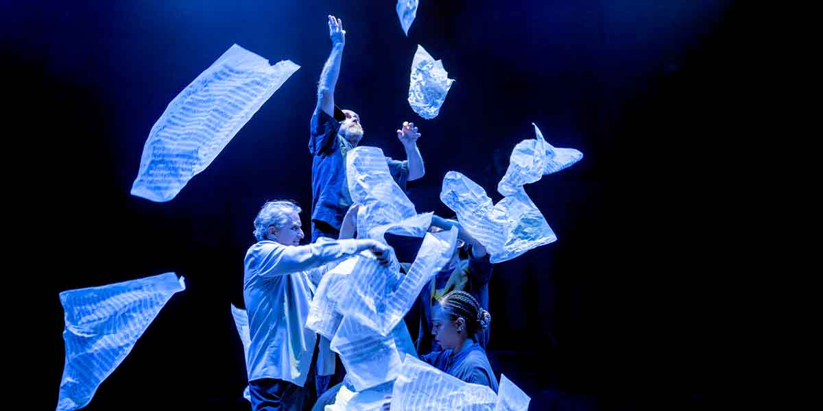 Phelim McDermott and three performers interact with translucent sheets, illuminated by blue stage lighting.