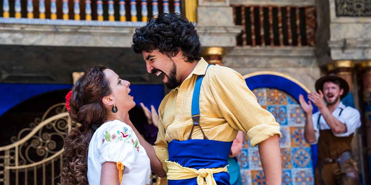 Suzanne Ahmet as Katherine and Pablo Egea smile at each other, with a vibrant stage backdrop.