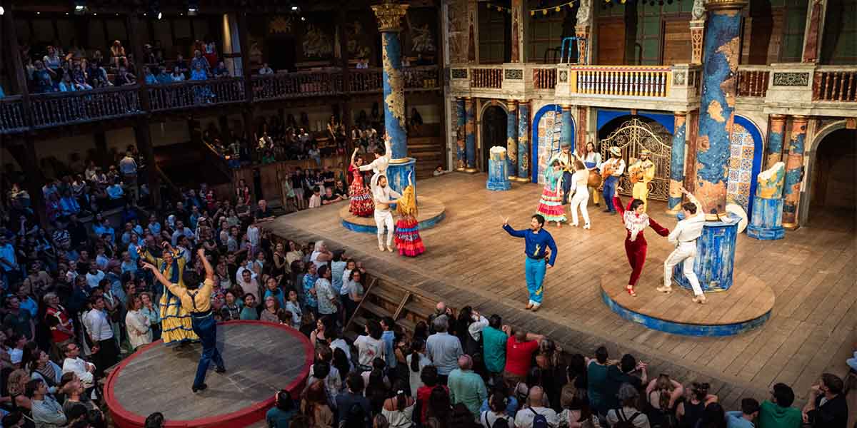 The cast of Love's Labour's Lost poses together on stage at Shakespeare's Globe, wearing period costumes.