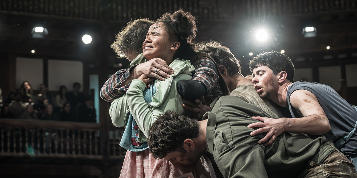 The cast of Mother Courage and Her Children performs on stage at Shakespeare's Globe, dressed in period costumes.