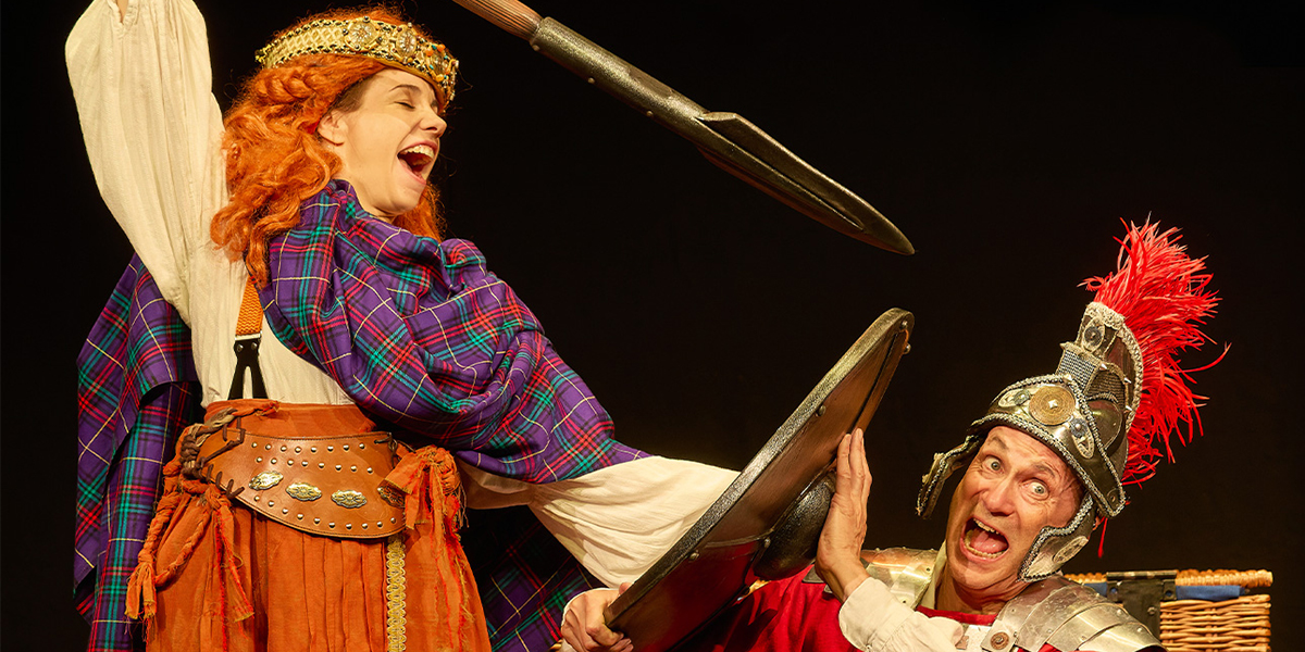 Children dressed in historical costumes perform a scene from Horrible Histories: Barmy Britain on stage.